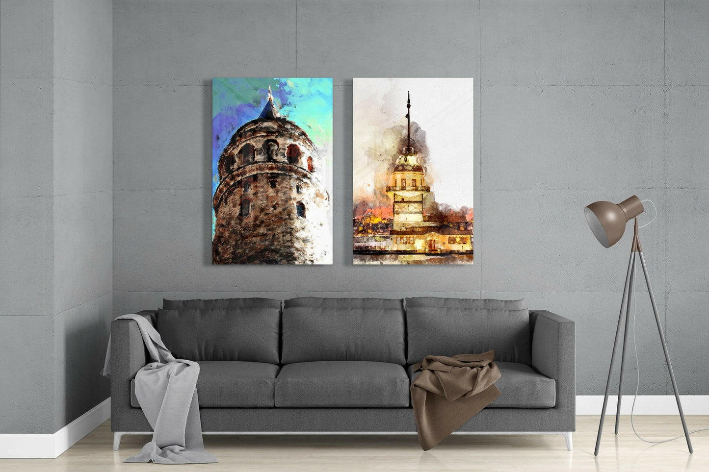 Two glass wall art panels mounted above a gray sofa display watercolor paintings of Istanbul towers with vibrant blue and warm golden tones.