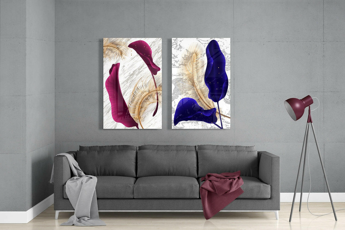 Two framed glass wall art pieces featuring burgundy and navy blue leaves with gold accents displayed above a gray sofa in a modern living room.