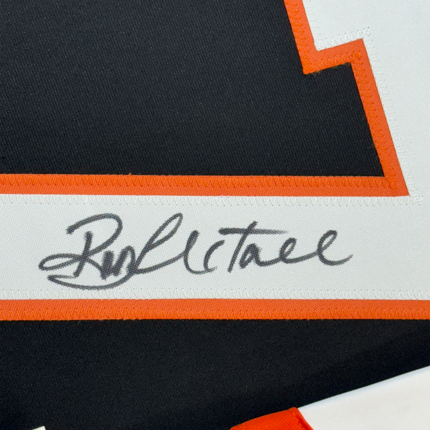 Close-up of Ron Hextall's handwritten signature on white stripe between orange and black fabric borders.