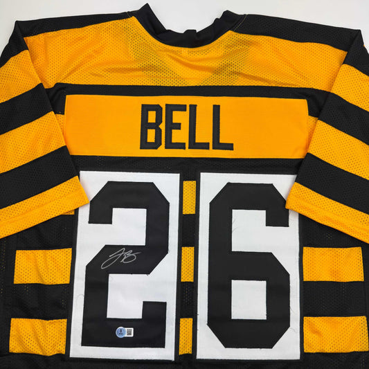 Flat lay of black and gold striped Pittsburgh Steelers jersey displaying "BELL" nameplate and number "26" with visible autograph.