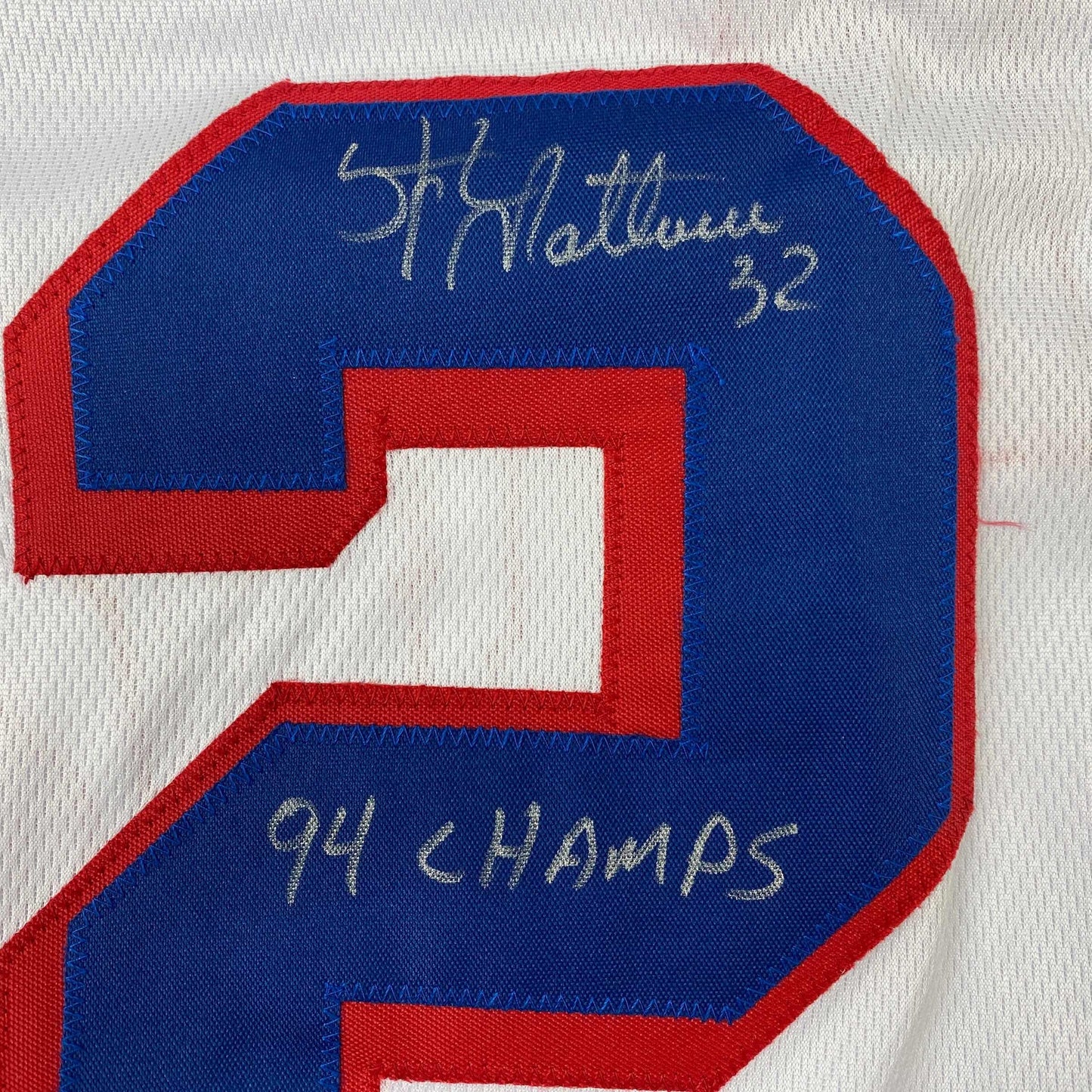 Close-up of blue and red hockey jersey number 2 with handwritten autograph and "94 CHAMPS" text on fabric.