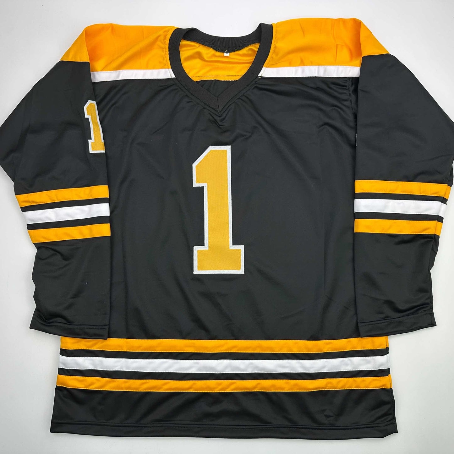Black Boston Bruins hockey jersey with gold number 1, gold and white shoulder stripes, displayed flat against white background.