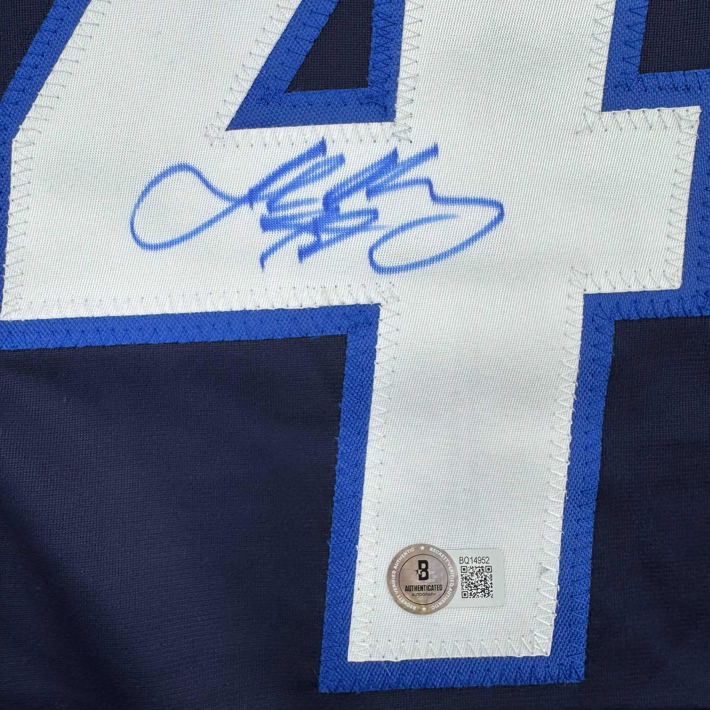 Close-up of blue autographed hockey jersey showing signed nameplate with Beckett authentication sticker and QR code.