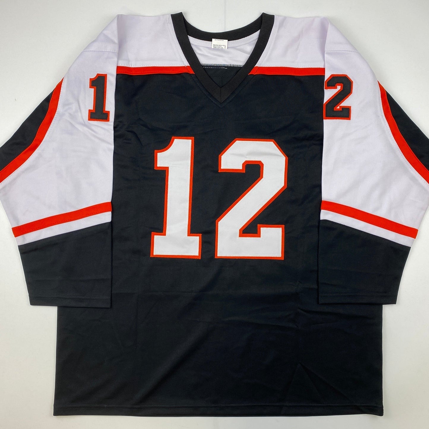 Black hockey jersey with red and white trim displaying number 12 in red and white on front, laid flat against white background.