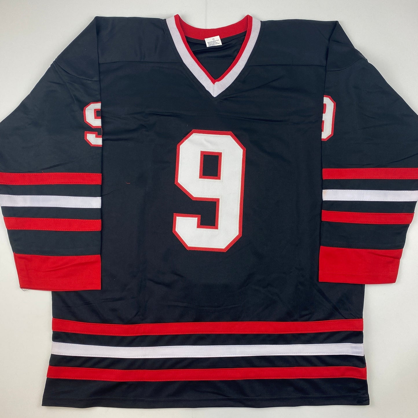 Black Chicago hockey jersey with red and white stripes, number 9 on chest, displayed flat against white background.