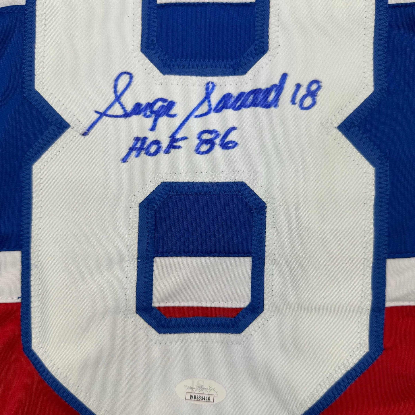 Close-up of signed blue and white hockey jersey showing autographed inscription "Serge Savard 18 HOF 86" and large number zero.