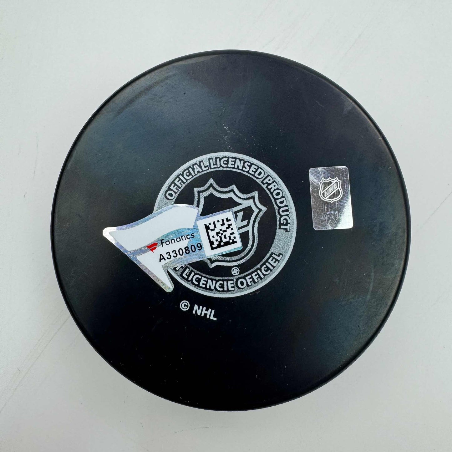 Top-down view of a black NHL hockey puck with official licensing seal, Fanatics barcode label, and NHL shield hologram sticker.