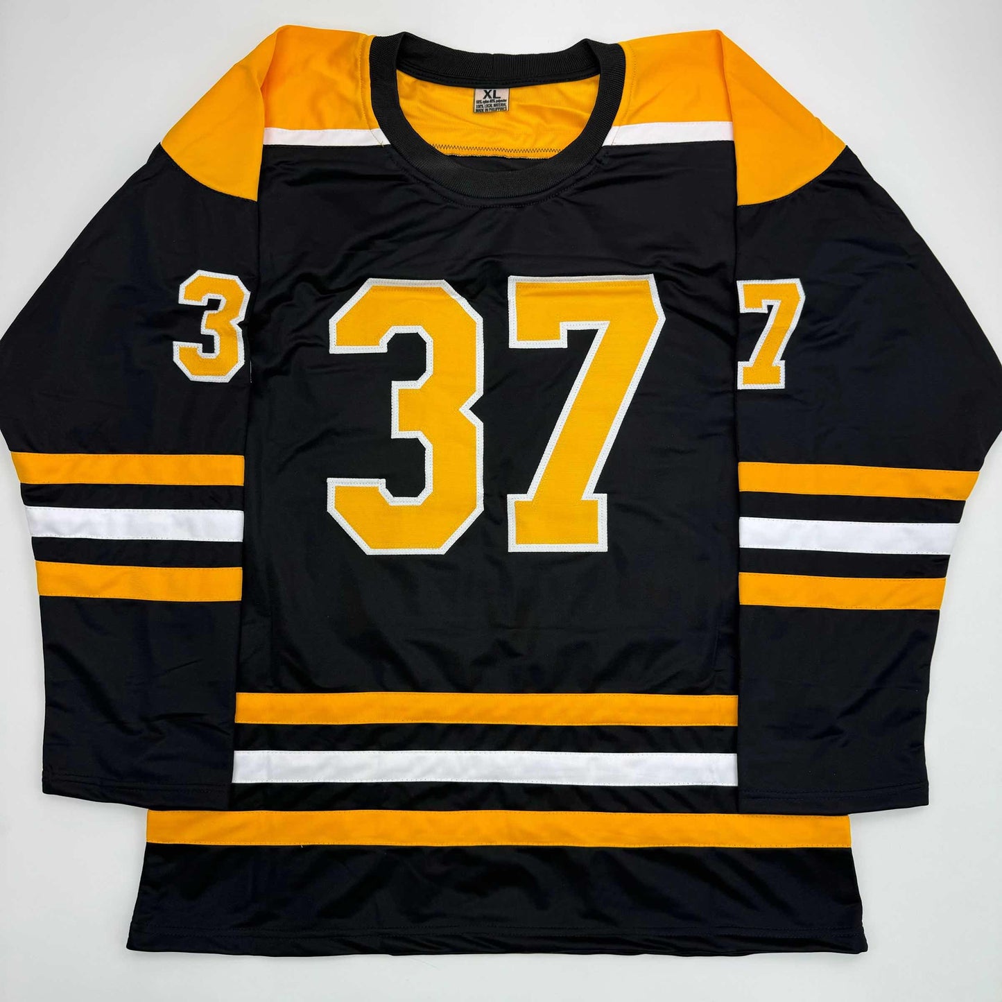 Flat lay of black hockey jersey with gold and white stripes, displaying number 37 on front chest.