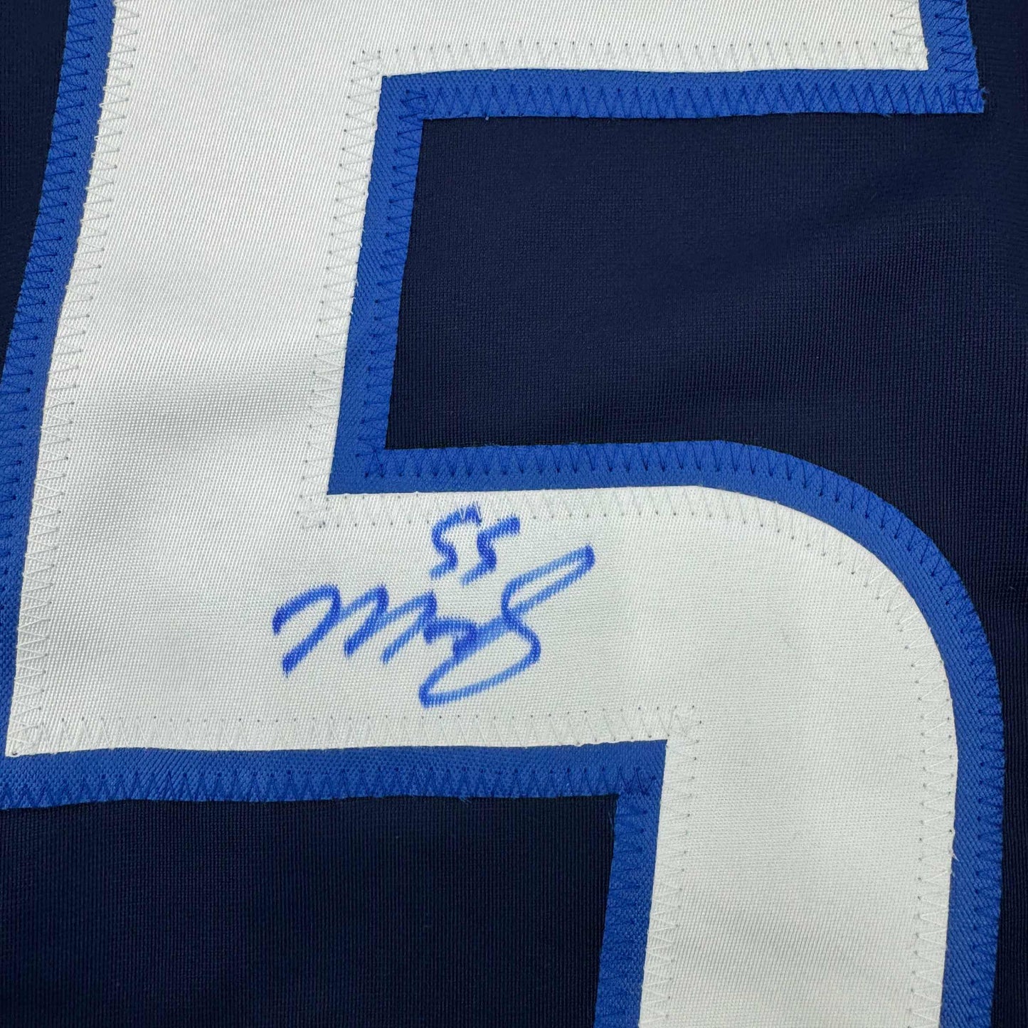Close-up of blue pen autograph on white curved corner section of navy and blue hockey jersey.