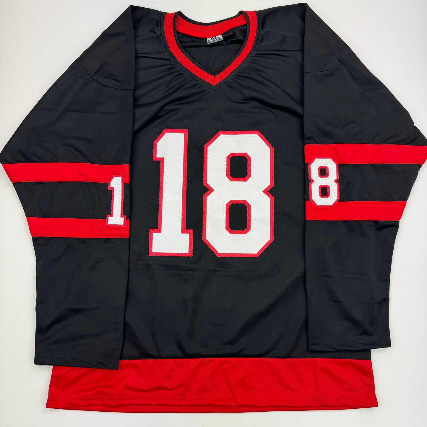 Black hockey jersey with red horizontal stripes, red V-neck trim, and white number 18 displayed flat on white background.