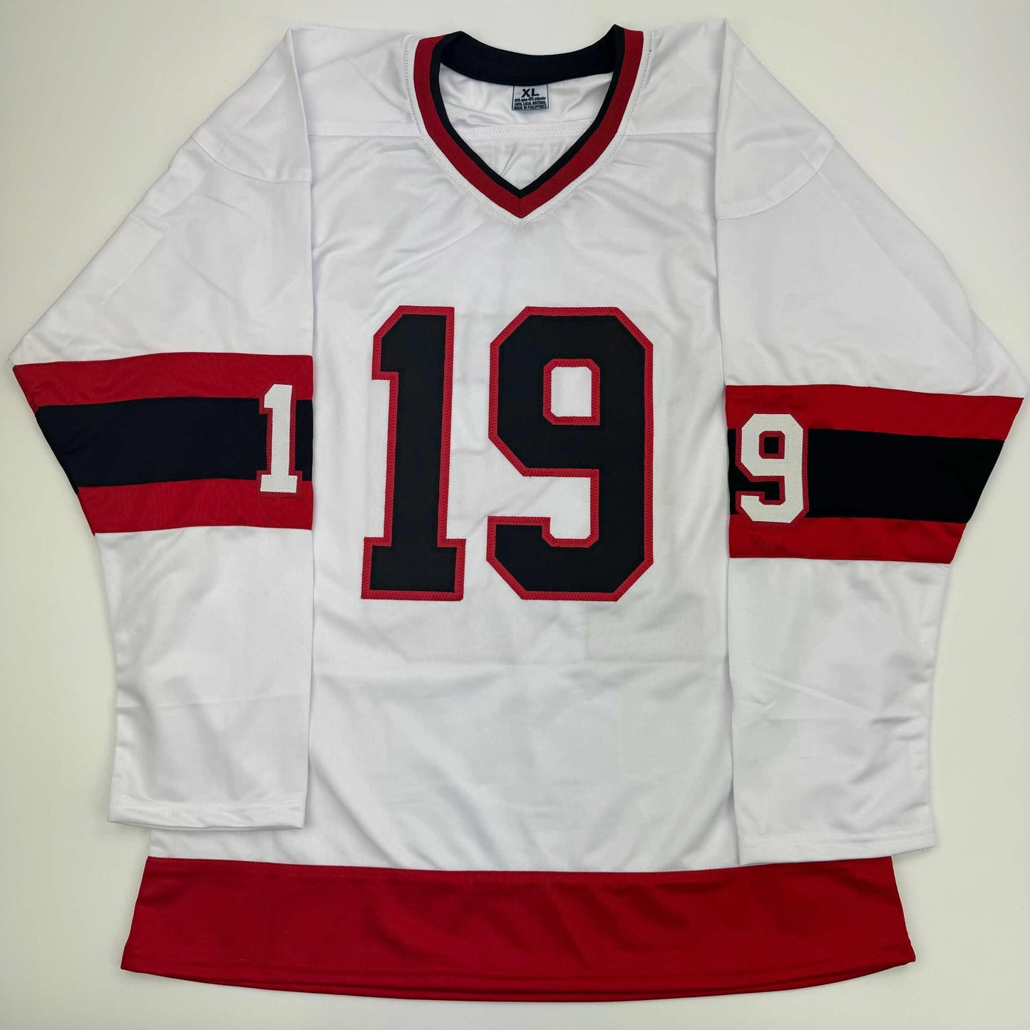 White hockey jersey with red and black striped sleeves, displaying black number 19 with red outline on chest, laid flat against white background.