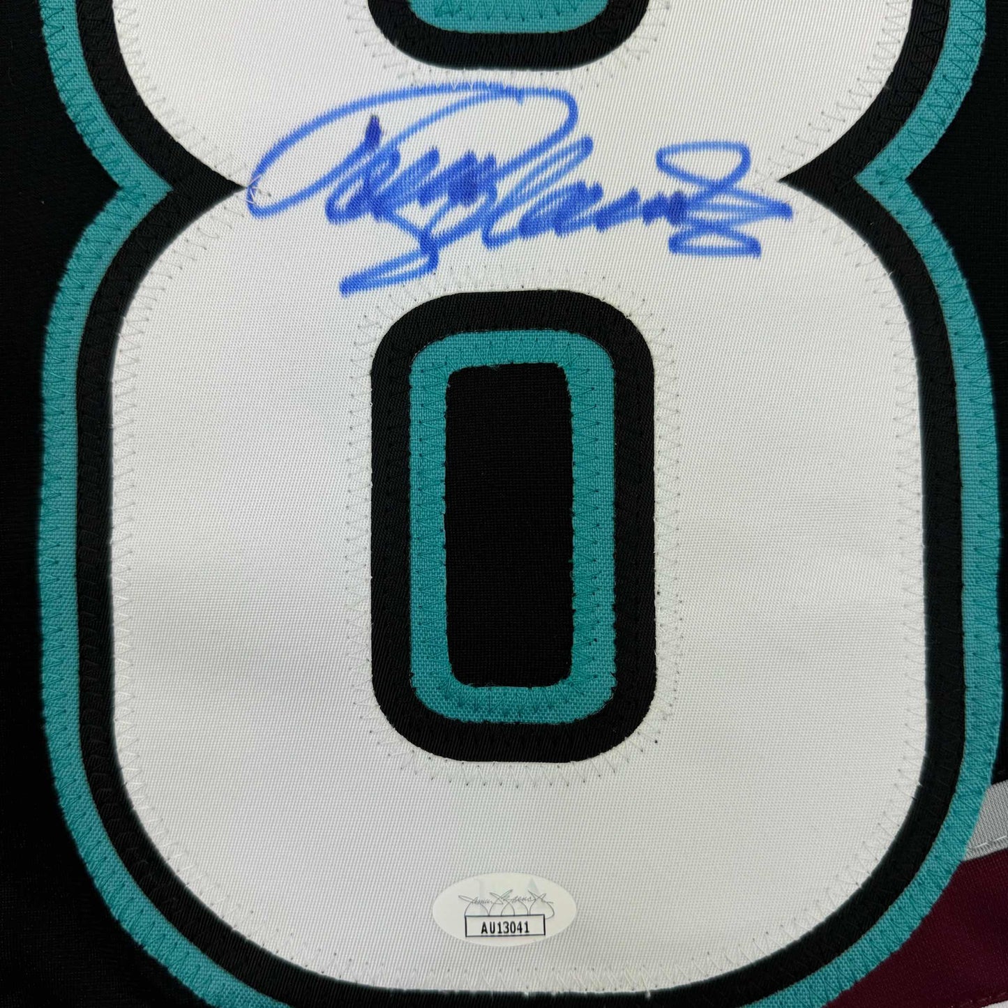 Close-up of signed Anaheim Ducks retro hockey jersey front showing number zero, teal and black trim, with blue autograph and authentication label.