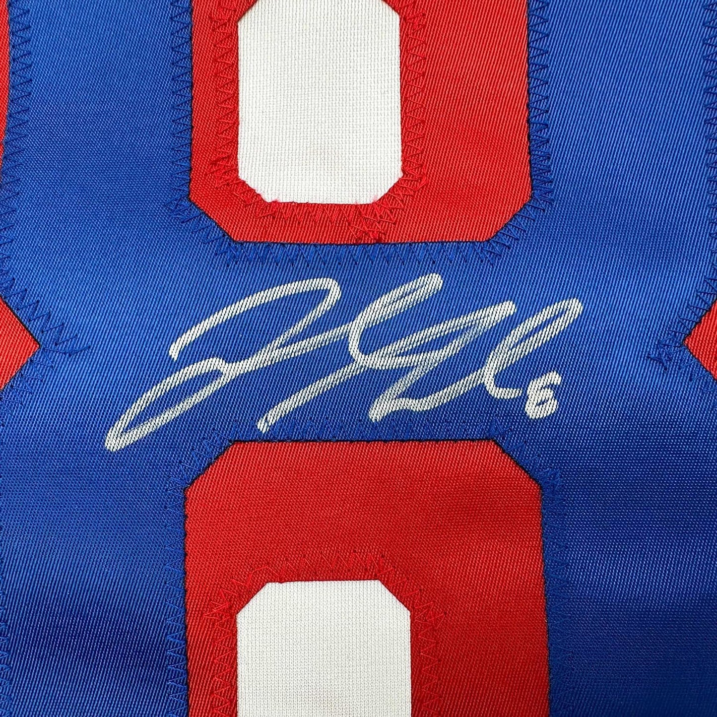 Close-up of white autographed signature on blue jersey fabric with red and white striped shoulder details.