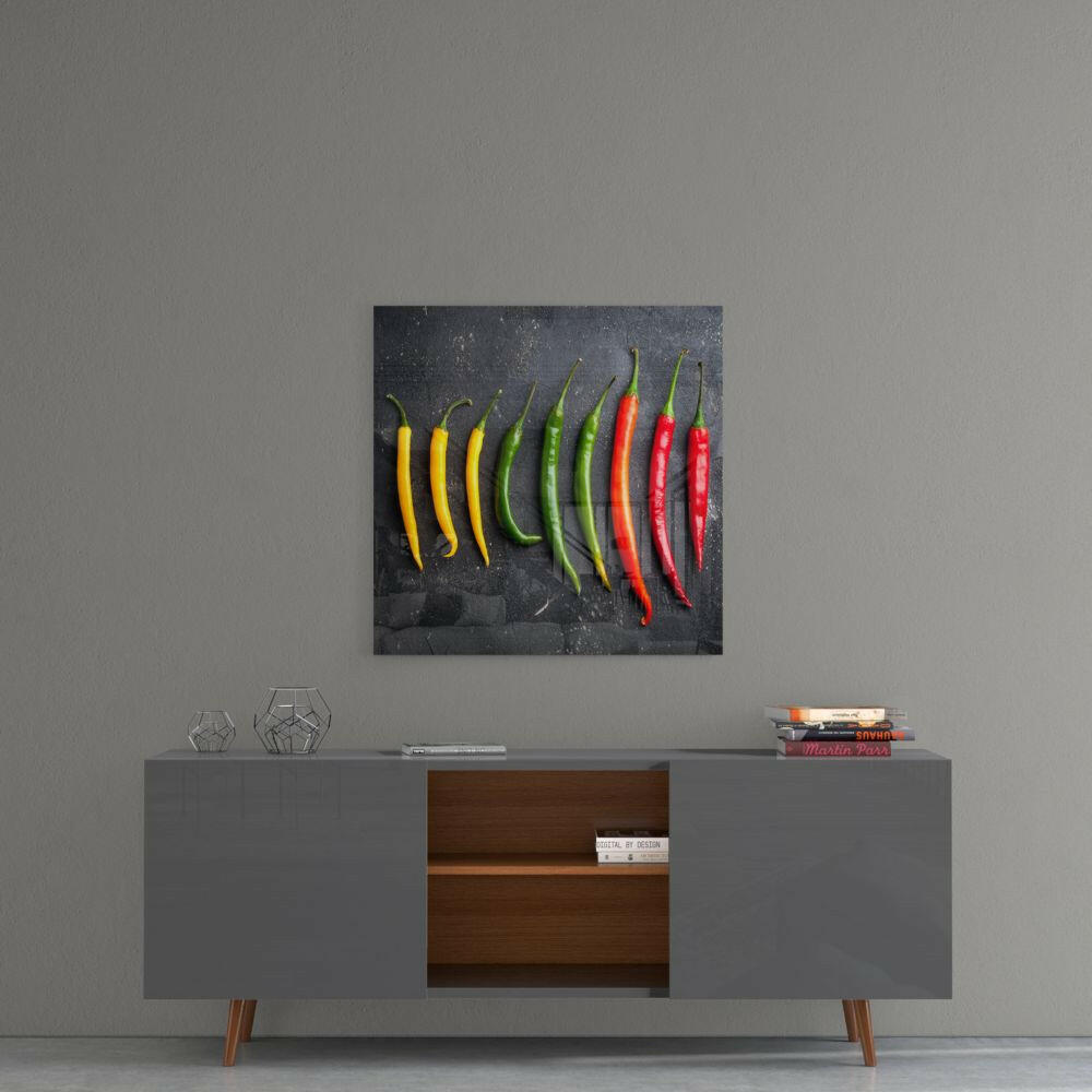 Square glass wall art featuring ten chili peppers arranged in gradient from yellow to red on dark textured background, displayed above gray mid-century modern credenza.