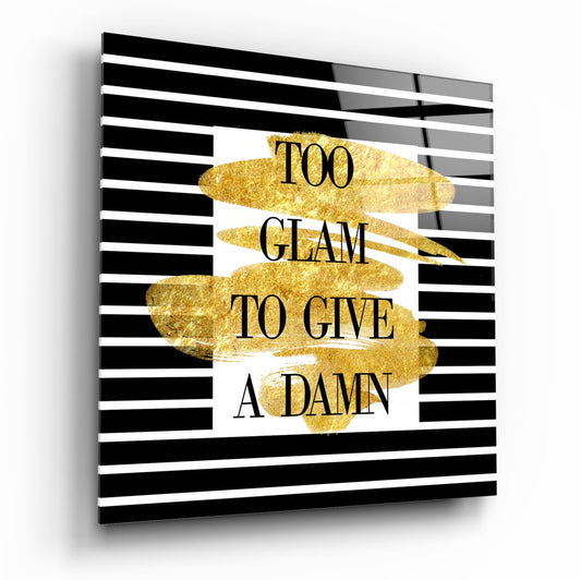 Angled view of glass wall art with black and white horizontal stripes, gold brushstroke shapes, and text reading "TOO GLAM TO GIVE A DAMN.