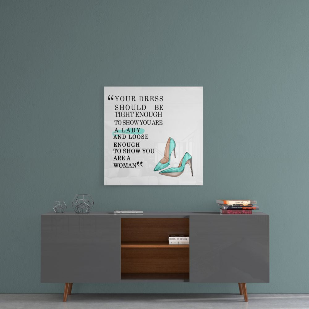 Glass wall art with fashion quote and turquoise high heels displayed above mid-century modern console table against blue-green wall.