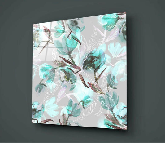 Angled view of teal and mauve watercolor magnolia glass wall art mounted on gray wall, showing translucent floral design with leaf details.
