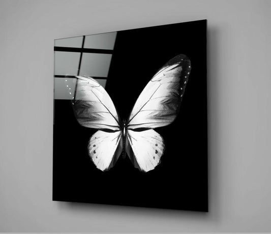 Black glass wall panel displaying a white butterfly with detailed wing patterns, mounted at an angle against a gray wall showing reflection.