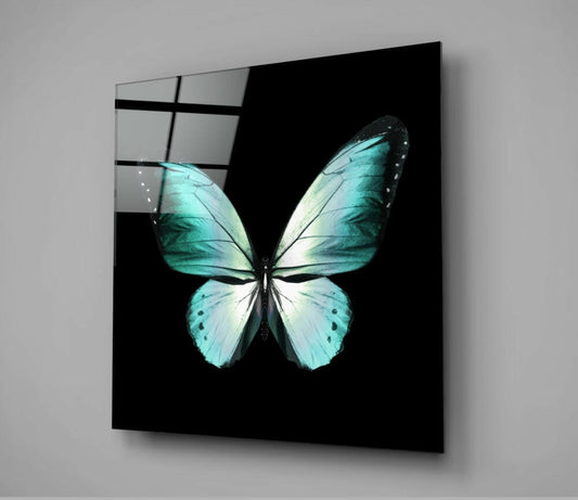 Angled view of turquoise and white butterfly glass wall art with black frame against gray wall.