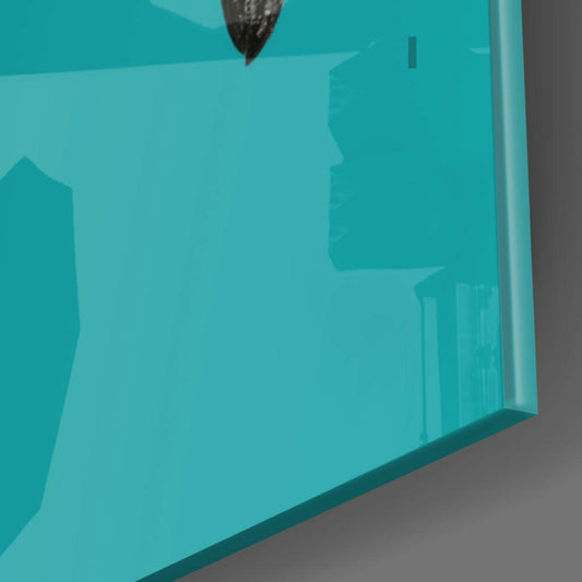 Close-up angled view of teal glass wall art showing smooth surface with darker shadowed silhouette shapes visible through translucent material.