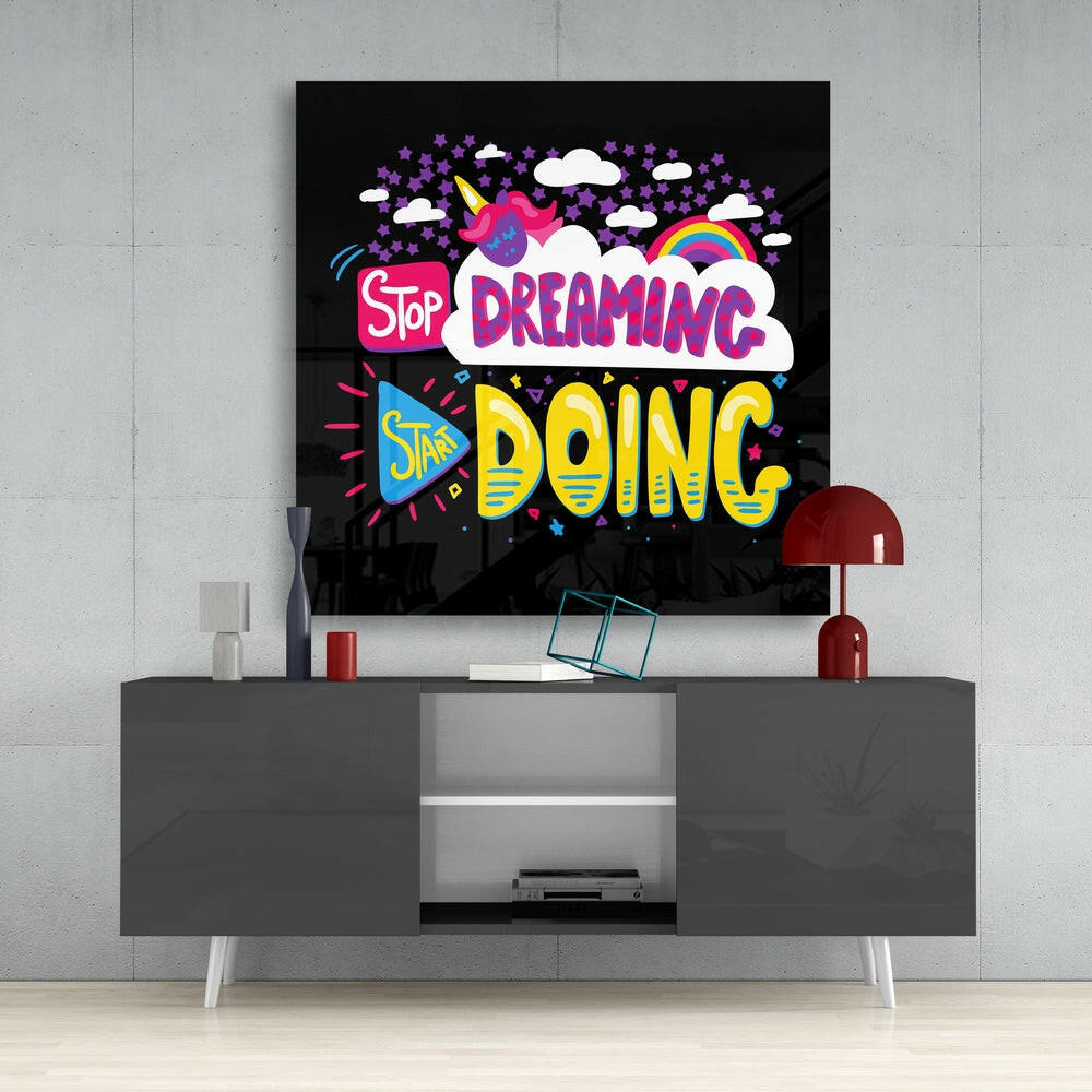 Colorful glass wall art with "Stop Dreaming Start Doing" text displayed above gray media console in modern living room setting.