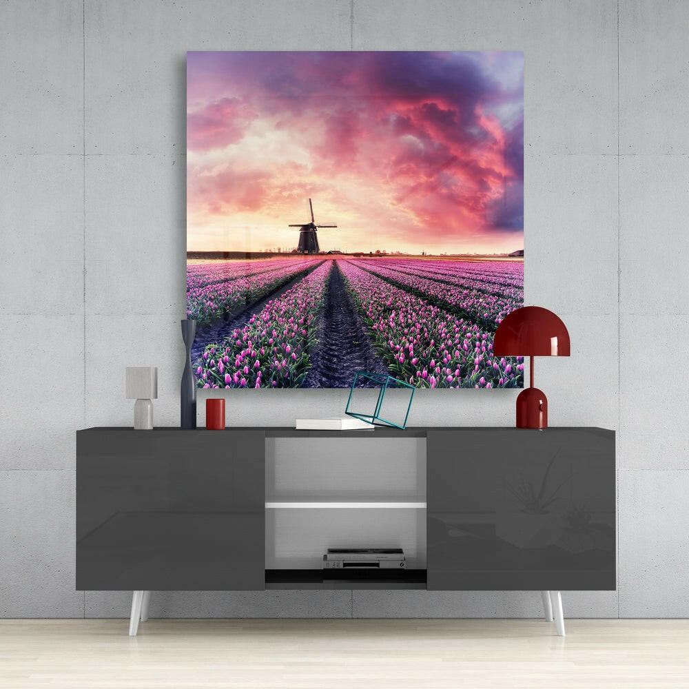 Glass wall art print displaying purple tulip fields with a windmill under dramatic pink and purple sunset sky, mounted above a gray media console.