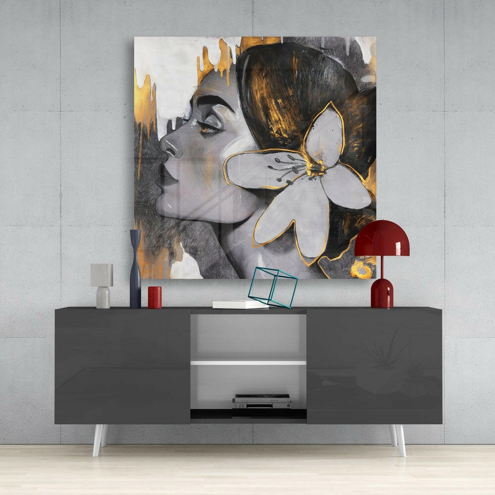 Modern interior display featuring a glass wall art panel with a woman's profile, gold accents, and white flower design mounted above a gray media console.