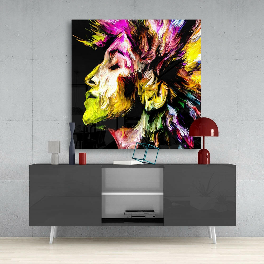 Colorful abstract portrait glass wall art displayed above gray media console, featuring vibrant magenta, yellow, and black streaked paint effect.