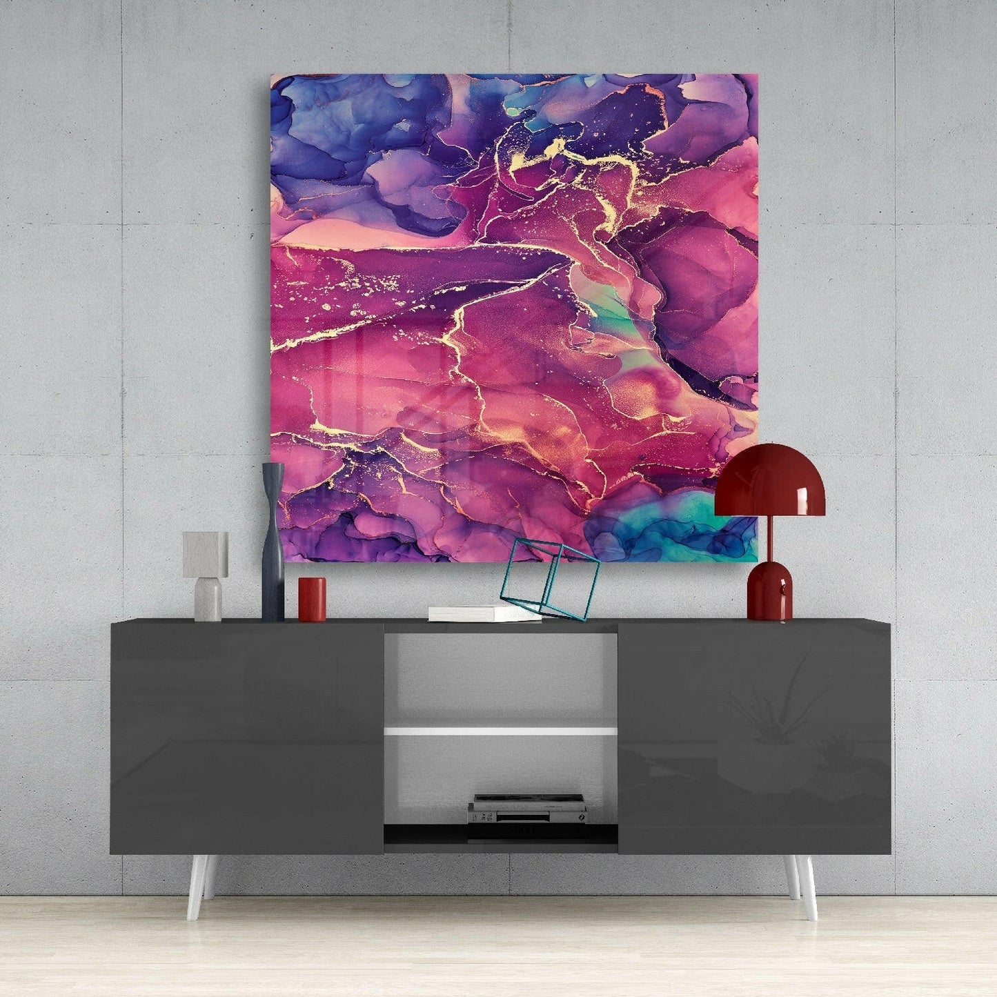 Abstract pink and gold marbled glass wall art hanging above a gray media console with red decorative objects.