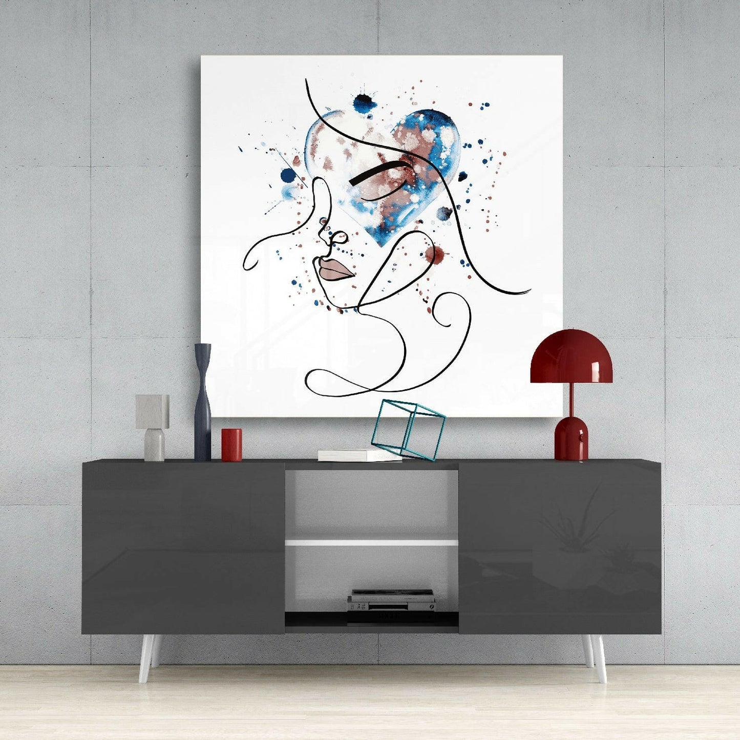Abstract line-drawn face with blue and burgundy watercolor splashes displayed above gray media console with red lamp and accessories.
