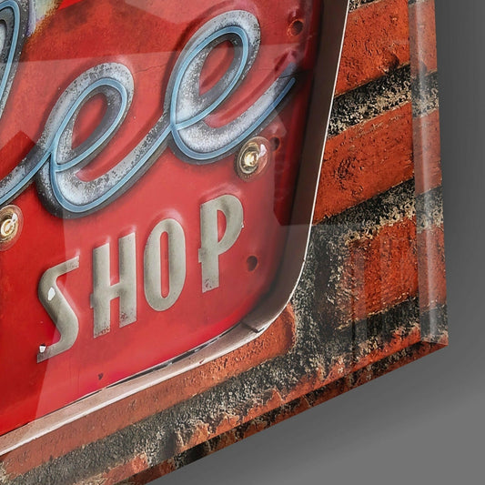 Close-up of red vintage coffee shop tin sign mounted on red brick wall, showing decorative loops and "SHOP" text with weathered metal finish.