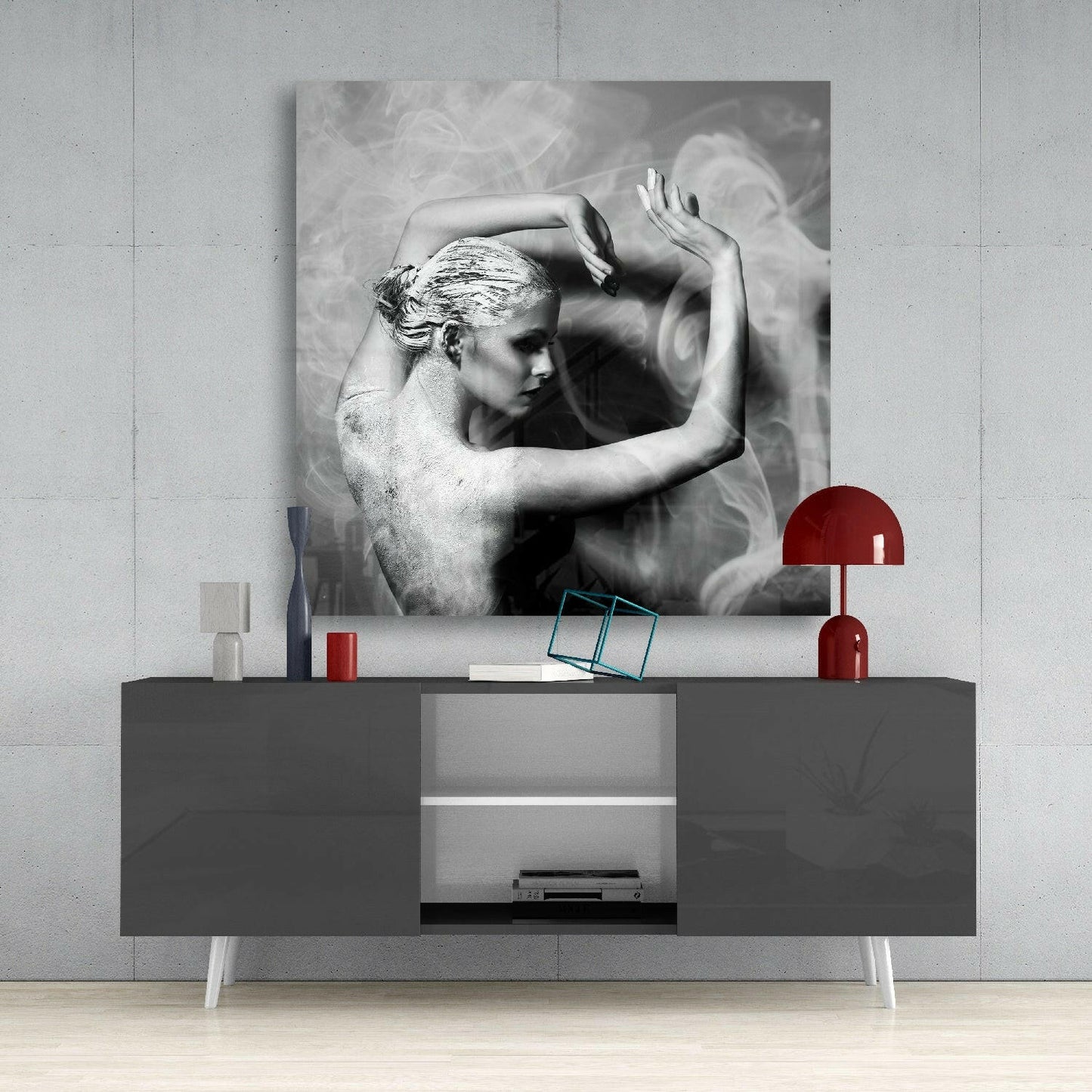 Black and white glass wall art depicting a shirtless man with styled hair and raised arms, displayed above a gray media console with red accents.