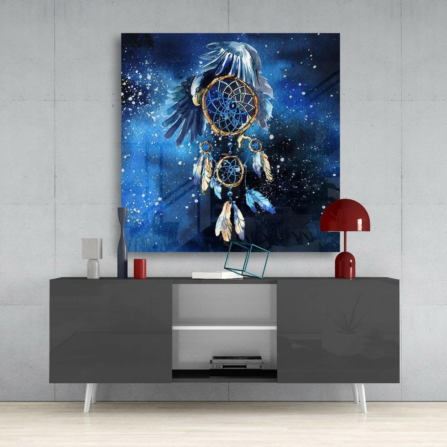 Blue dreamcatcher glass wall art with eagle and feathers displayed above gray media console with red lamp.