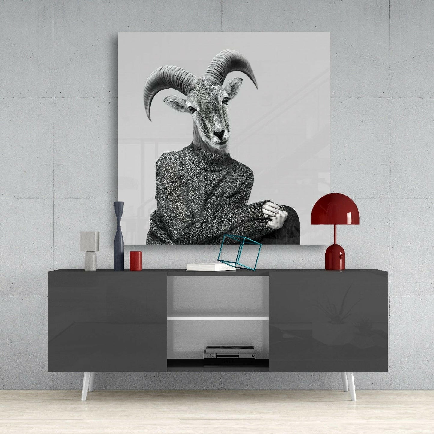 Black and white glass wall art depicting an anthropomorphic antelope in a sweater, displayed above a dark console table with red lamp and accessories.