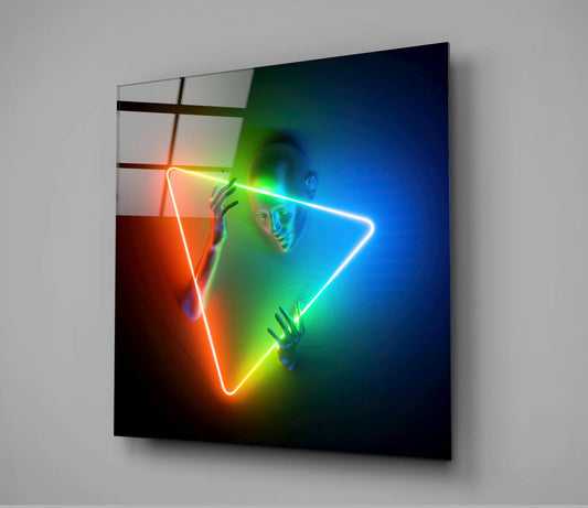 Glass wall art panel with neon rainbow triangle outline framing a figure's face, displayed at an angle against gray wall.