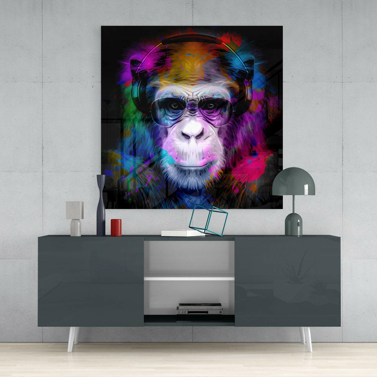 Colorful glass wall art of a chimpanzee wearing headphones and sunglasses displayed above a gray media console in a modern interior setting.