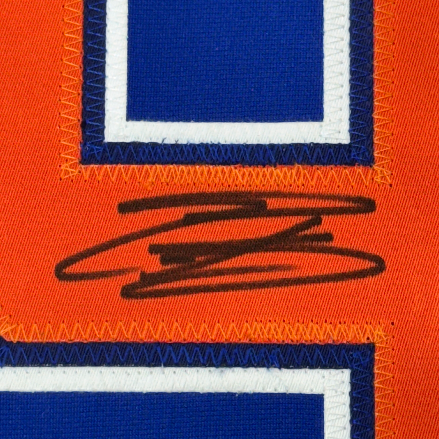 Close-up of autographed jersey detail showing black signature on orange fabric with blue and white striped borders.
