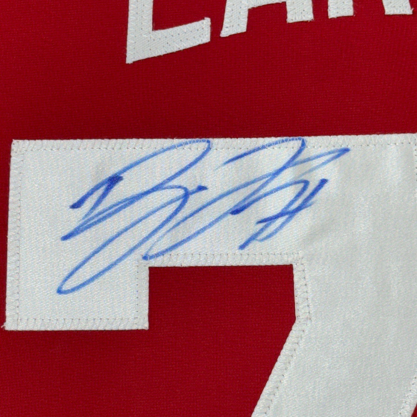 Close-up of blue autographed signature on white nameplate strip of red hockey jersey.