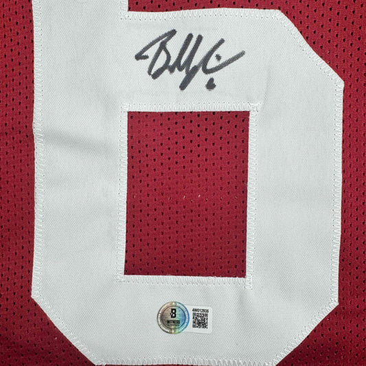 Close-up of signed white mesh jersey front with red fabric swatch and handwritten signature, showing Beckett authentication hologram and QR code.