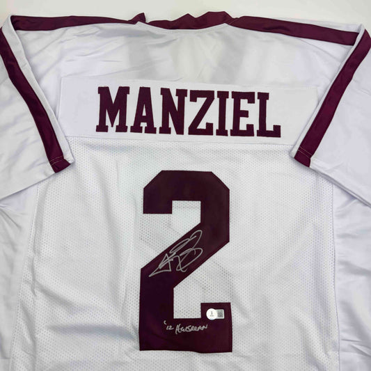 Flat-lay close-up of a white jersey back with a maroon MANZIEL nameplate, maroon number 2, and a silver signature above "'12 Heisman.