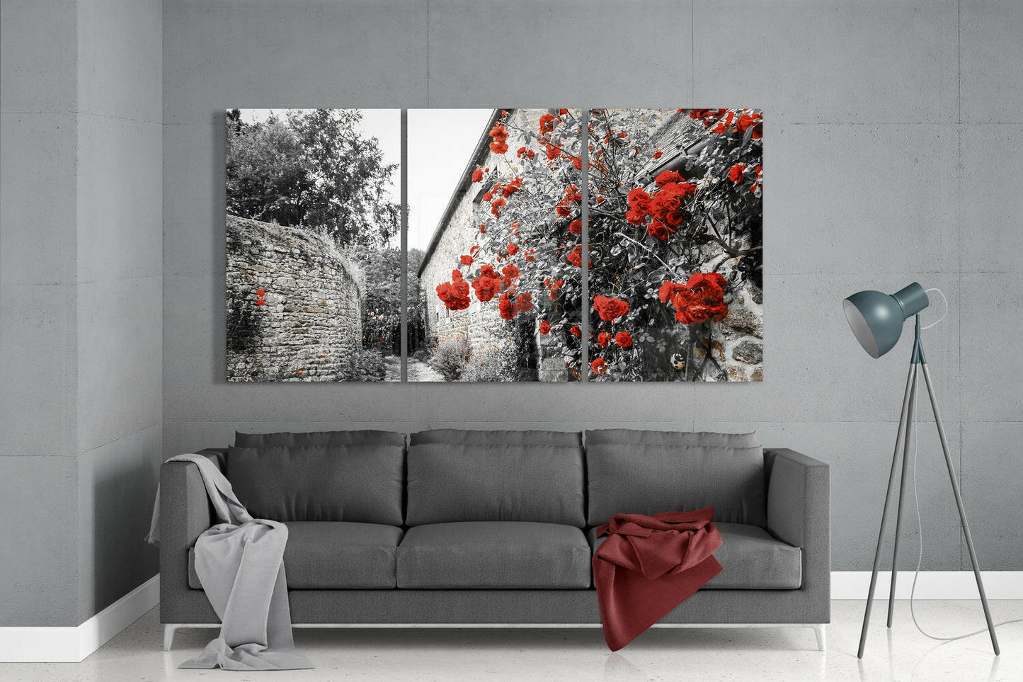 Three-panel glass wall art displaying black and white stone architecture with vibrant red flowers, hung above gray sofa in modern living room.