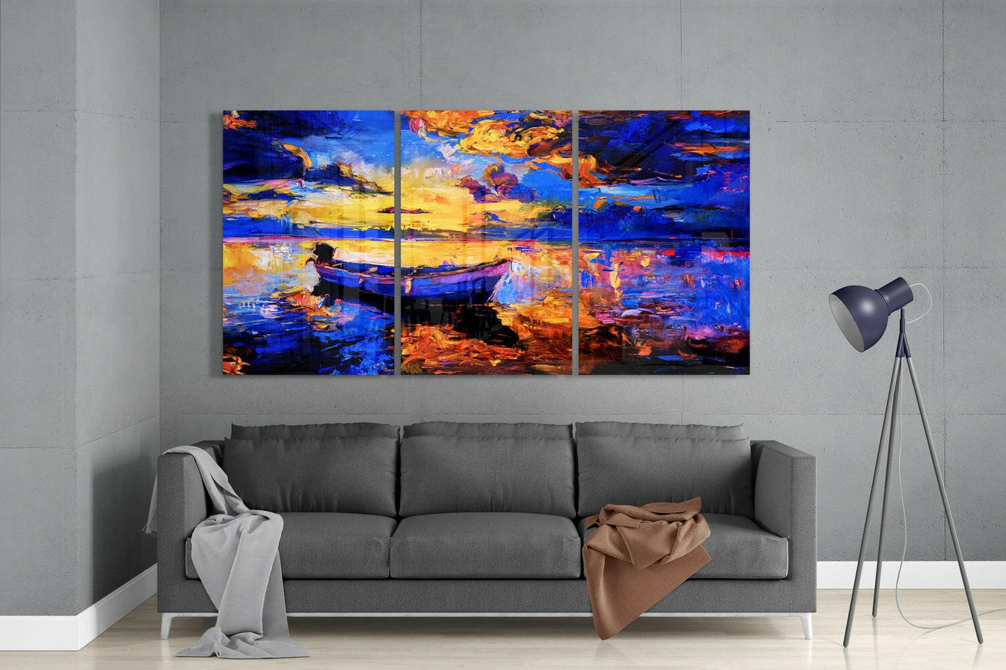 Three-panel vibrant glass artwork depicting a blue boat at golden sunset, displayed above gray sofa in modern living room interior.