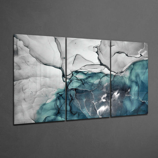 Three-panel glass wall art displaying abstract marble patterns in teal, gray, and white tones mounted on gray wall.
