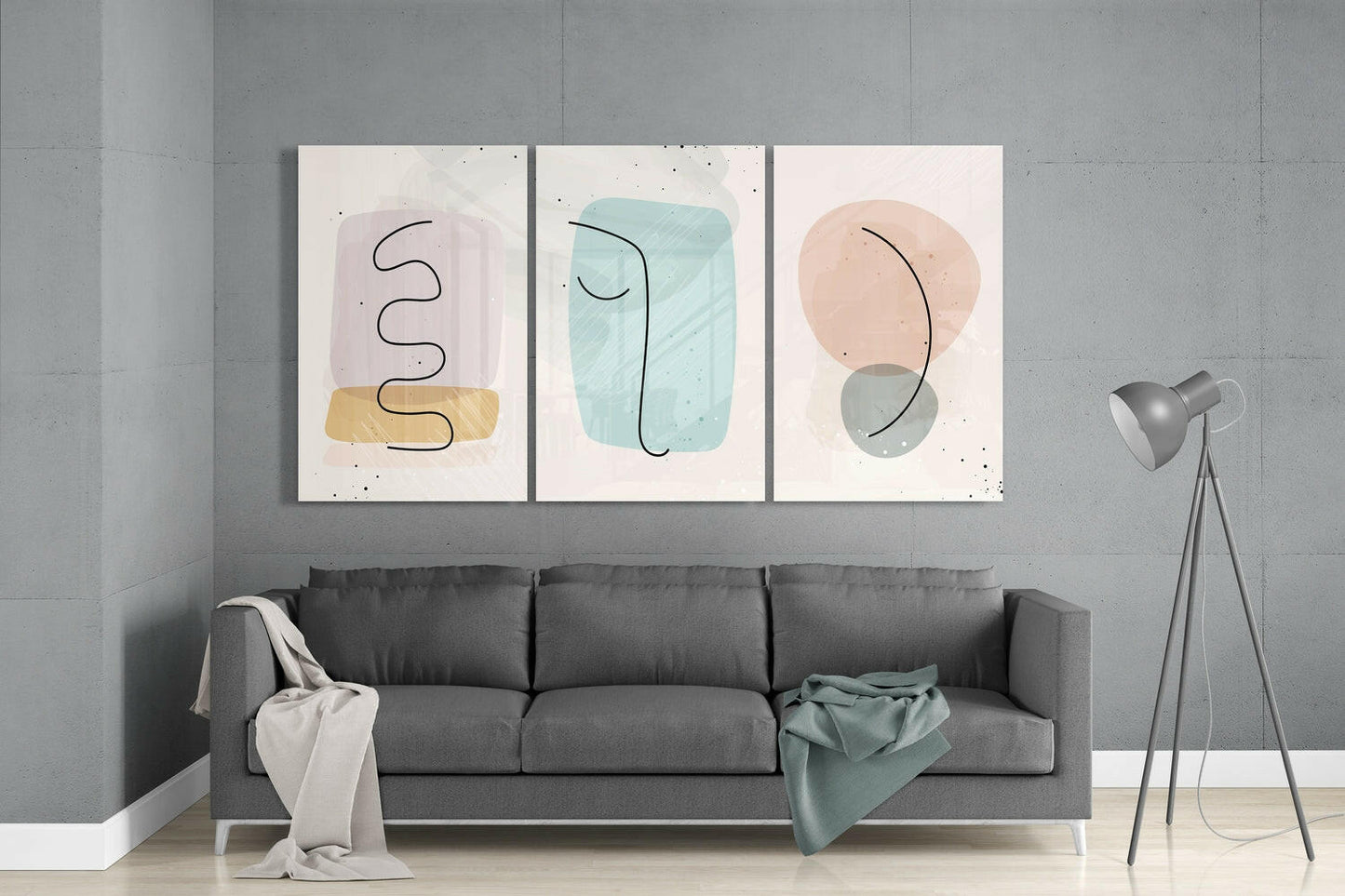 Three abstract glass wall art panels with pastel shapes and line drawings displayed above a gray sofa in a modern living room.
