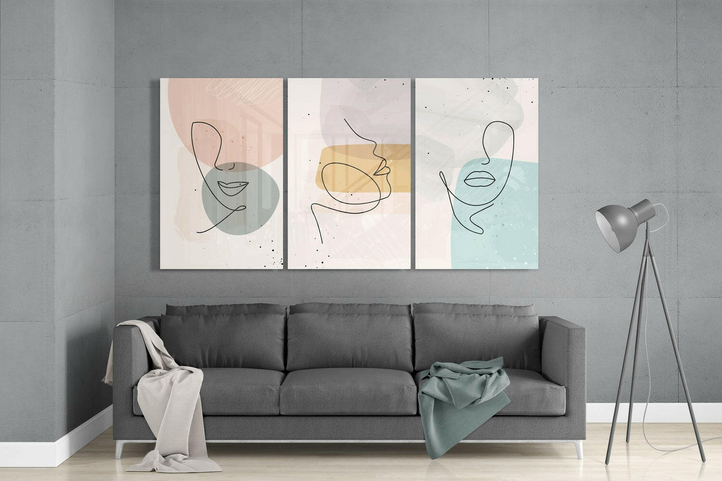 Three abstract line-drawn face glass panels in pastel pink, yellow, and blue displayed above a gray sofa in a modern living room interior.
