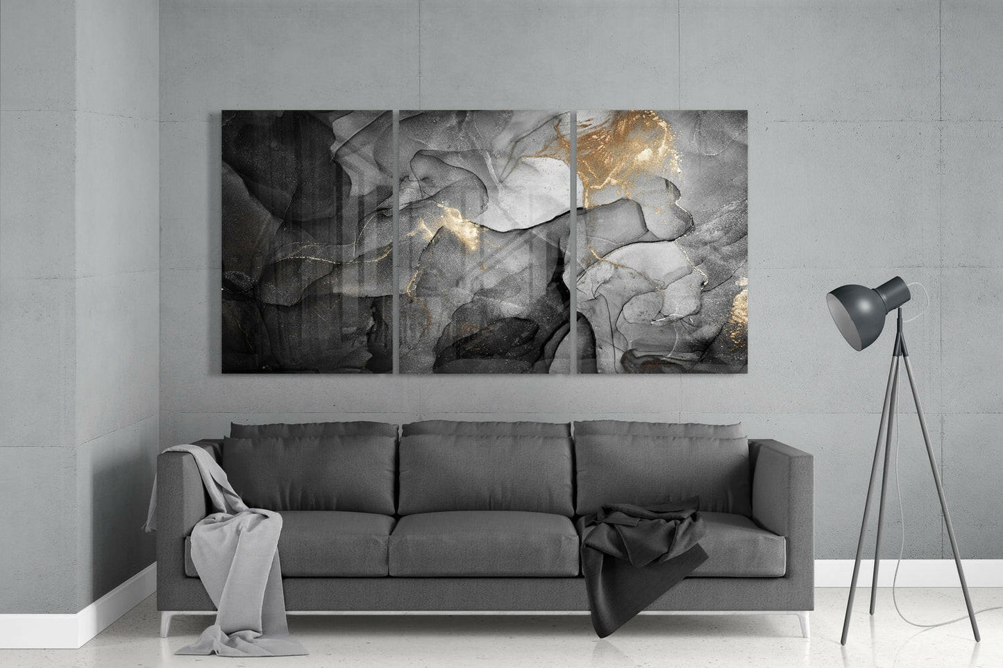 Three-panel abstract glass wall art with black, gray, and gold marbling hung above a gray sofa in a minimalist interior.