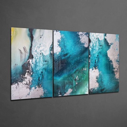 Three-panel glass wall art displaying turquoise, teal, and white poured paint patterns mounted on gray wall at angle.