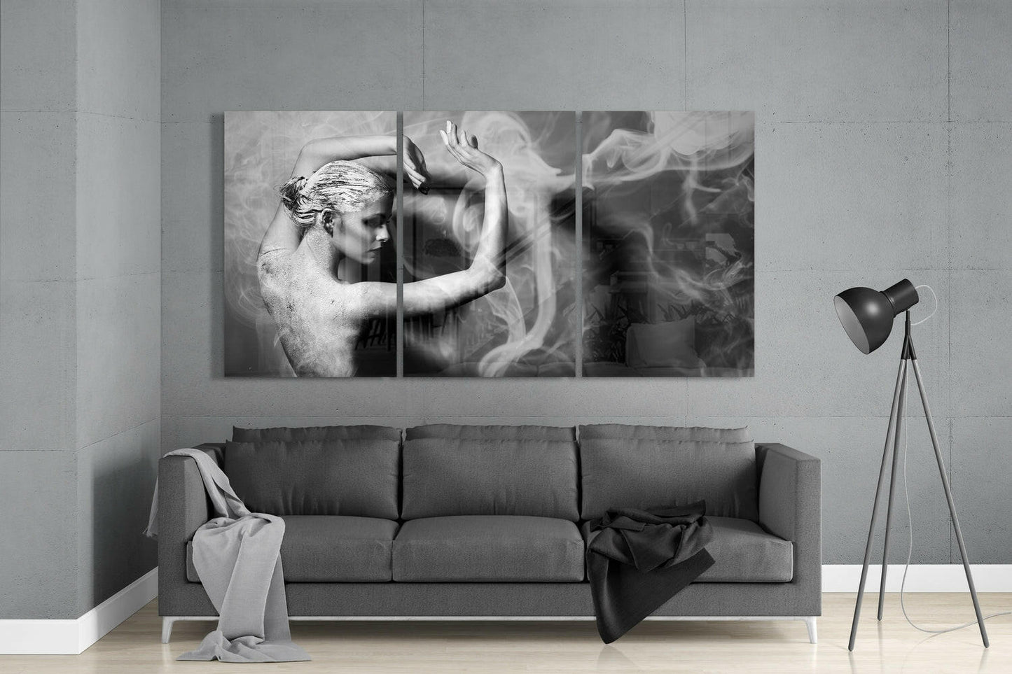 Three-panel black and white glass wall art mounted above gray sofa, depicting artistic figure with flowing fabric and raised arms.