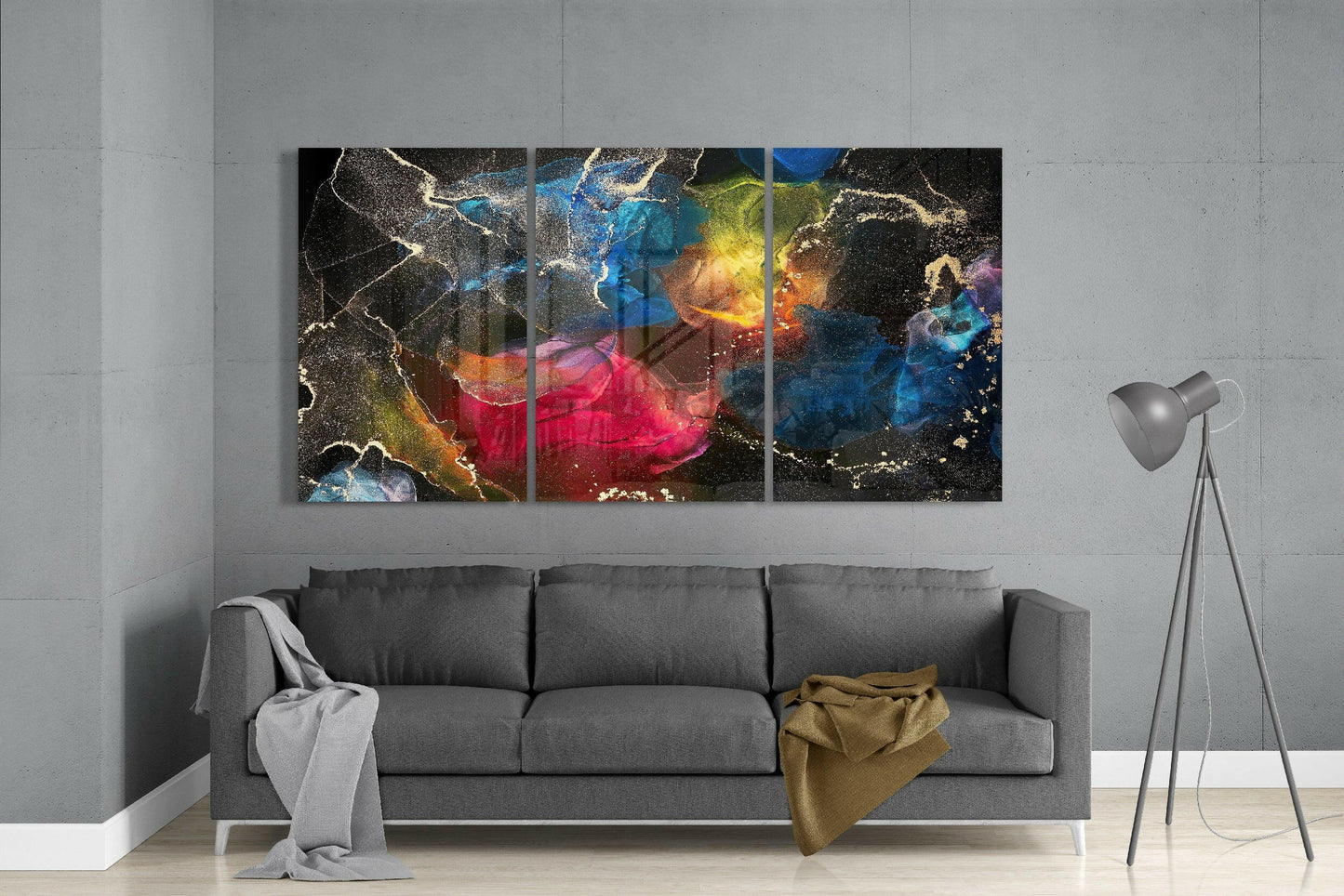 Three-panel colorful glass art with gold veins and vibrant blues, reds, and yellows displayed above gray sofa in modern living room.