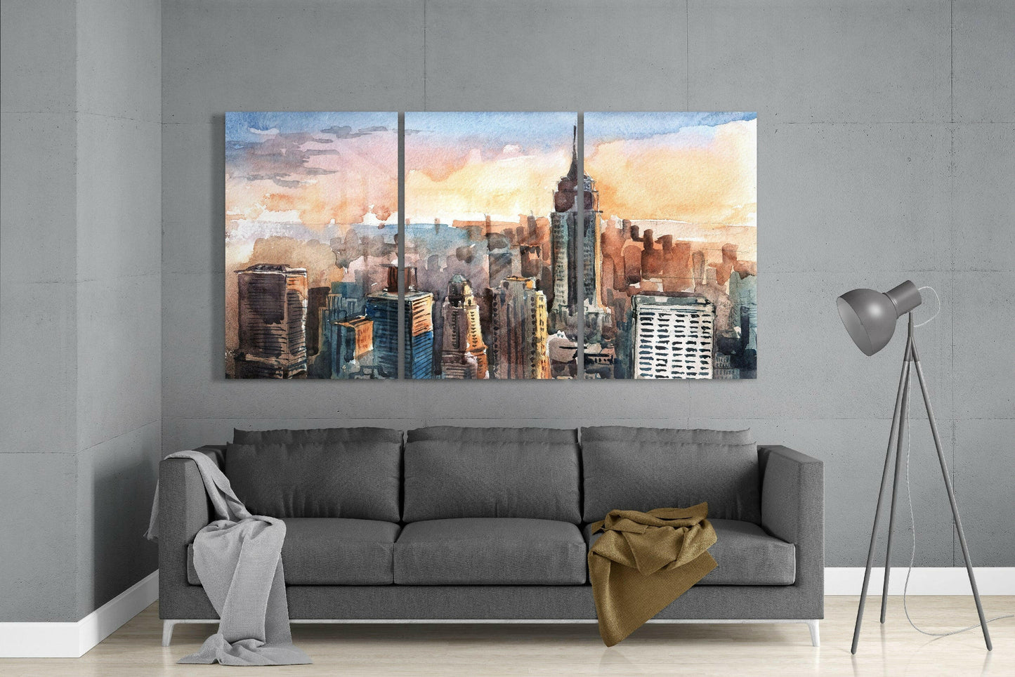 Three-panel watercolor Manhattan skyline glass art above gray sofa in modern interior setting.